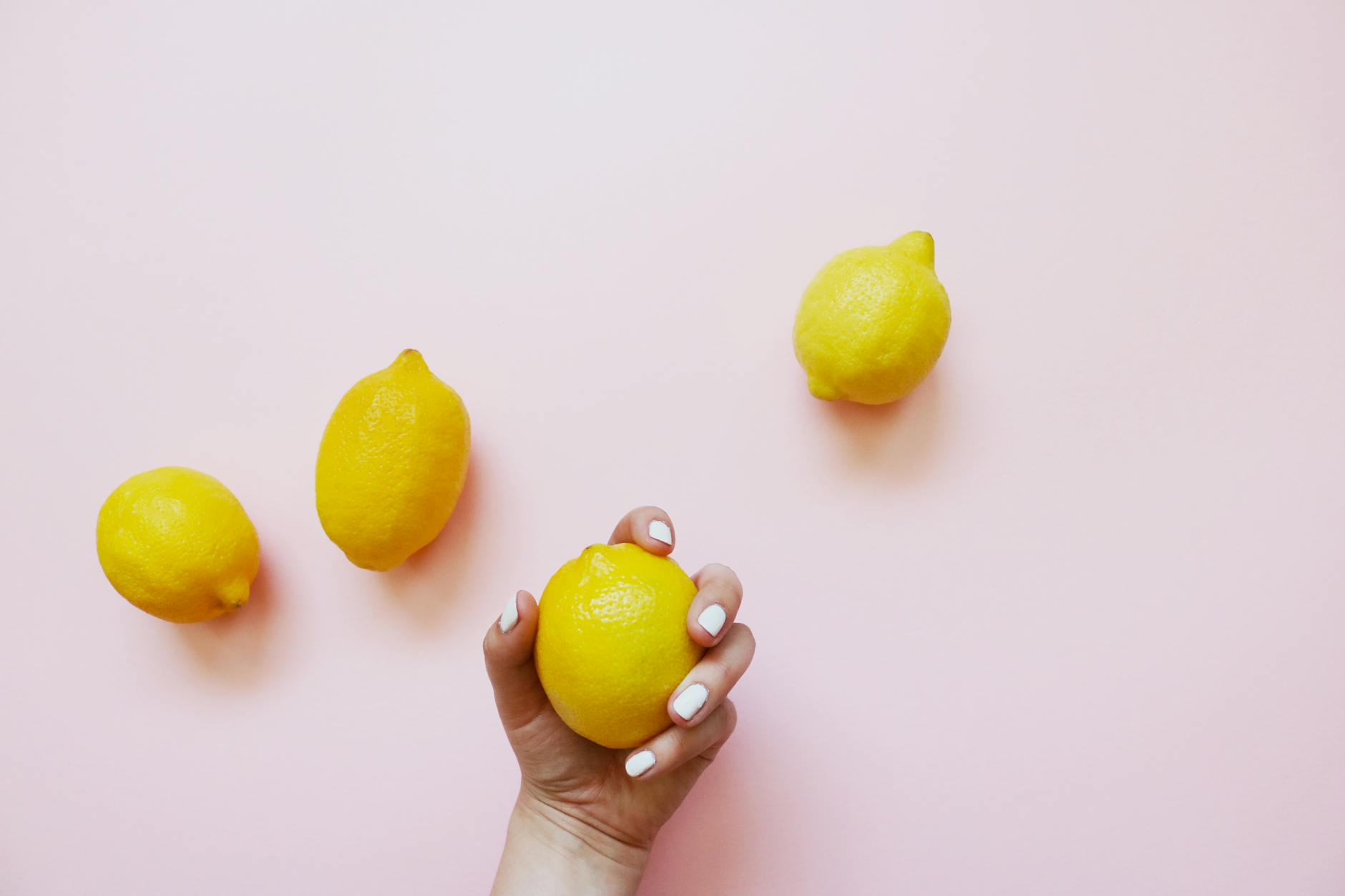 A hand holding a lemon on a soft pink background, symbolizing freshness and renewal in intimate moments