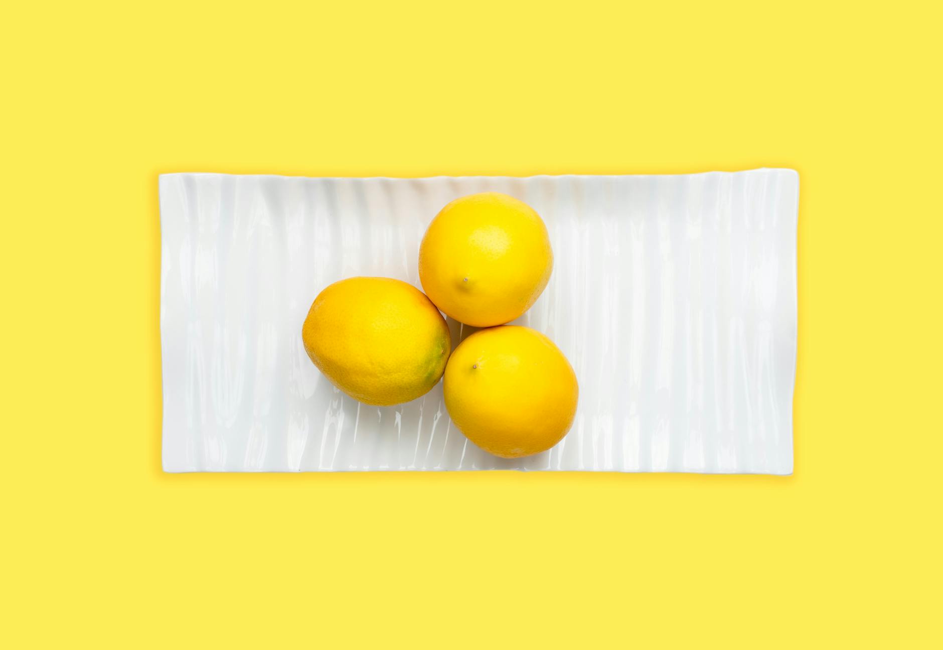 Fresh lemons on white plate with vibrant yellow background, symbolizing the freshness and sensitivity of youthful pleasure