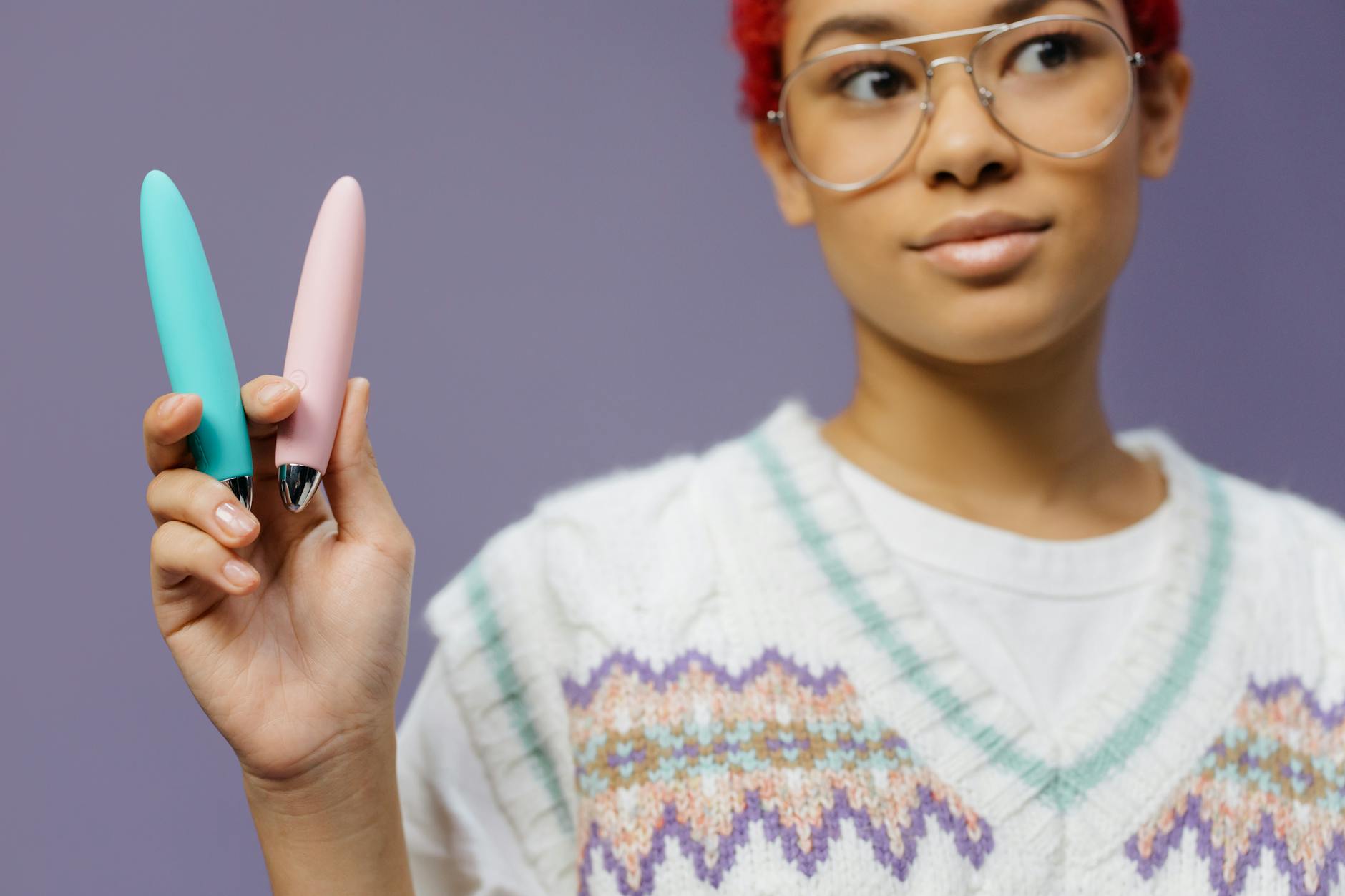 A blue silicone vibrator held in hand against a solid purple background