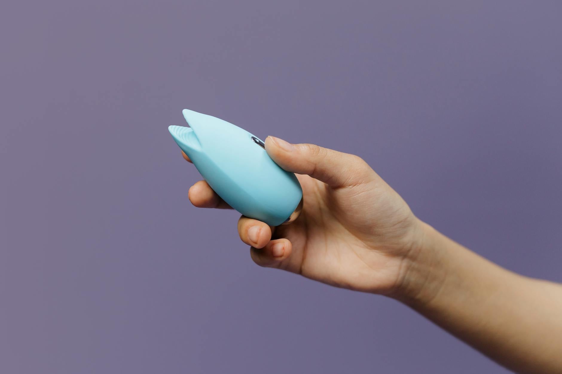 Blue silicone vibrator held in hand against purple background for self-pleasure and intimacy